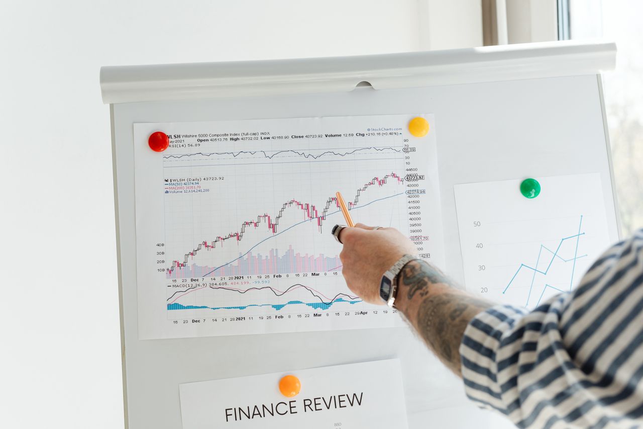 about-me A tattooed person pointing at finance charts and graphs on a whiteboard.