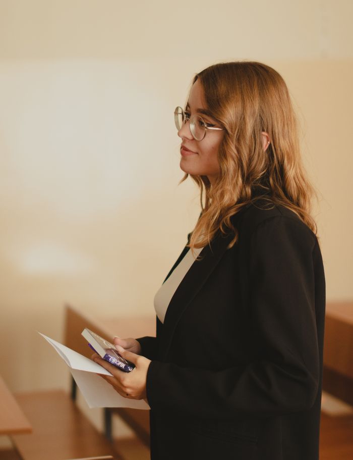 our-mission Profile of a young woman in glasses holding papers in a classroom setting.